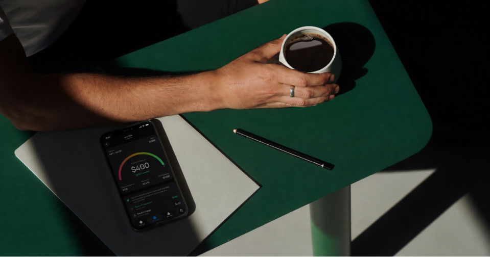 Phone with a Spread balance screen on a green desk beside coffee.