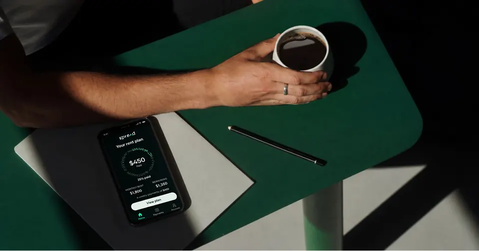 Phone with a Spread balance screen on a green desk beside coffee.